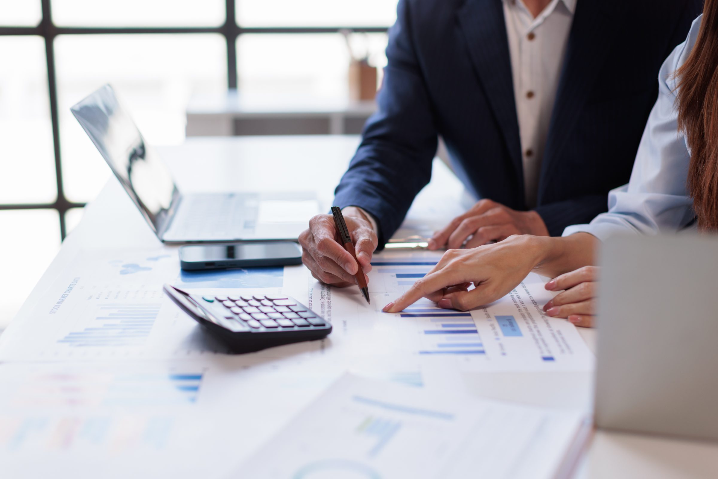 Two business professionals reviewing financial charts and graphs at a table with calculator and laptop