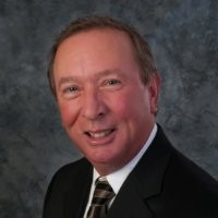 Professional headshot of a smiling man in a dark suit and striped tie