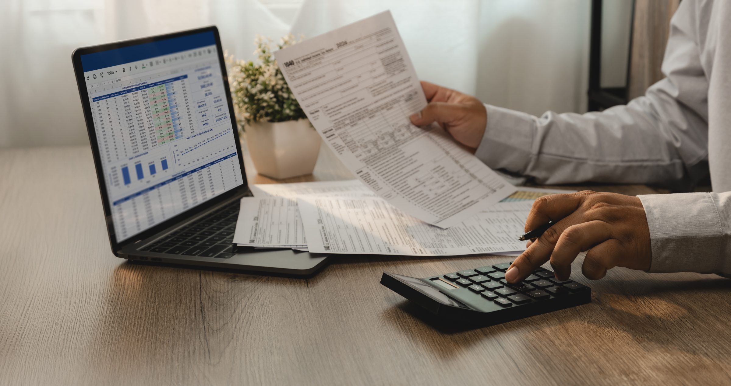 Business professional reviewing financial documents and spreadsheet data on laptop with calculator